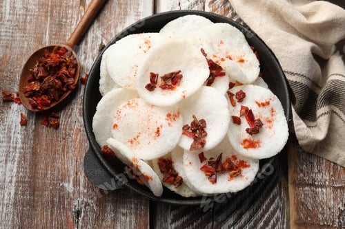 Preview: Tasty rice paper chips with spices in frying pan, spoon and napkin on color wooden table, flat lay