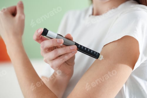 Preview: Diabetes. Woman making insulin injection into her arm with autoinjector indoors, closeup