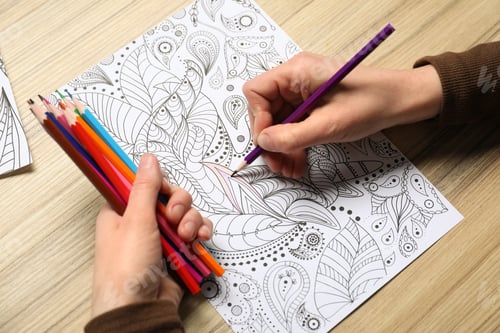 Preview: Woman coloring antistress picture with pencils at wooden table, closeup