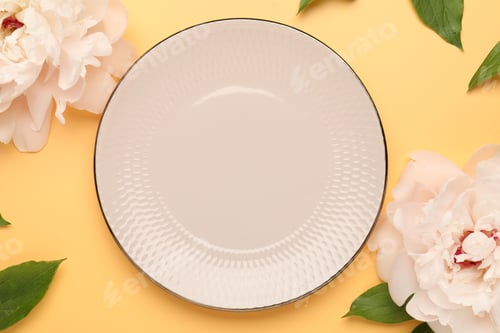 Preview: Stylish table setting with plate, flowers and green leaves on pale orange background, flat lay