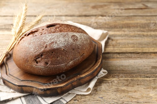Preview: Loaf of fresh bread and spikes on wooden table, closeup. Space for text
