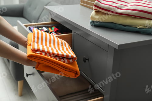 Preview: Woman putting folded clothes into drawer indoors, closeup