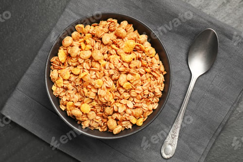 Preview: Tasty granola in bowl and spoon on black table, flat lay