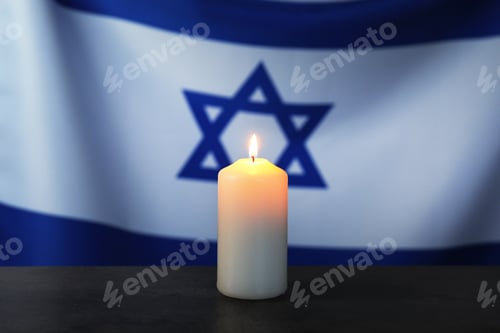 Preview: Holocaust Remembrance Day. Burning candle on dark table against flag of Israel