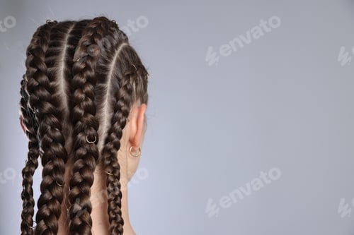 Preview: Teenage girl with beautiful braids on grey background, back view. Space for text