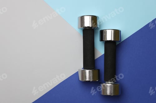 Preview: Two metal dumbbells on color background, flat lay. Space for text