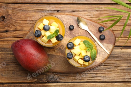 Preview: Delicious mango panna cotta with fruits and mint in glasses on wooden table, flat lay