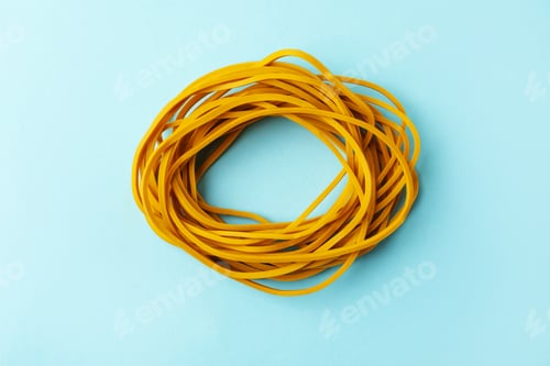 Preview: Many yellow rubber bands on light blue background, top view