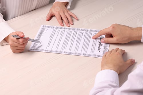 Preview: Man and woman signing marriage contract at light wooden table, closeup
