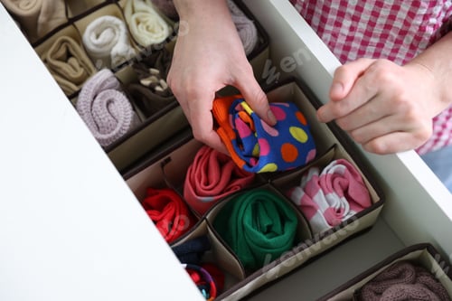 Preview: Woman putting socks into drawer with organizer indoors, closeup