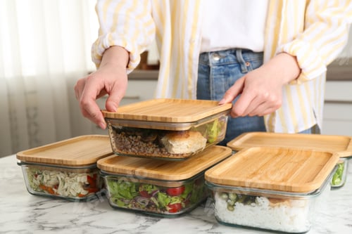 Preview: Healthy food. Woman closing glass container with meal at white marble table, closeup
