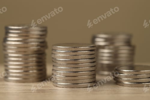 Preview: Stacks of coins on wooden table against dark beige background, closeup