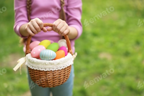 Preview: Easter celebration. Little girl holding basket with painted eggs outdoors, closeup. Space for text