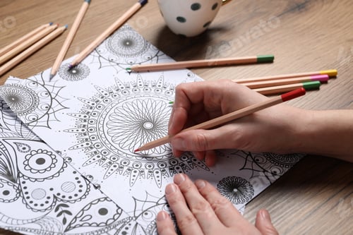 Preview: Woman coloring antistress picture with pencils at wooden table, closeup