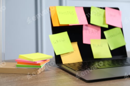 Preview: Computer with colorful sticky notes on wooden table, selective focus. Multitasking, deadline and rus