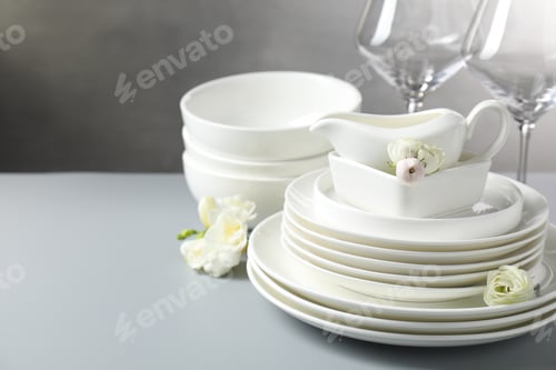Preview: Many clean dishware and beautiful flowers on grey table, closeup. Space for text