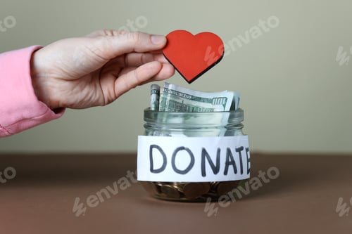 Preview: Woman putting red decorative heart into donation jar on color background, closeup
