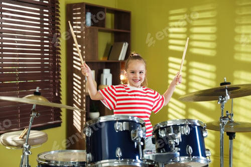 Preview: Smiling little girl learning how to play drums indoors