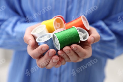 Preview: Woman holding spools of sewing threads indoors, closeup