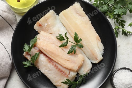 Preview: Plate with raw cod fish, parsley and salt on light table, flat lay