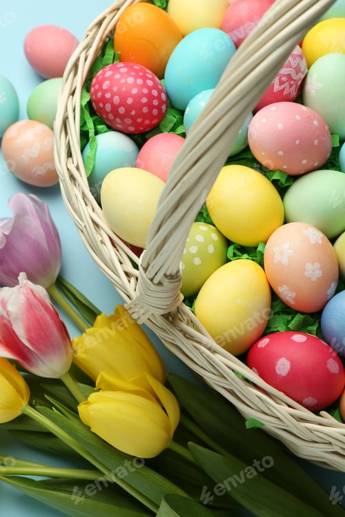 Preview: Easter basket with painted eggs and tulips on light blue background, flat lay