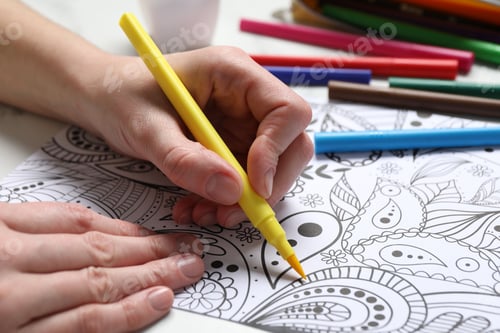 Preview: Woman coloring antistress picture with felt tip pen at white table, closeup