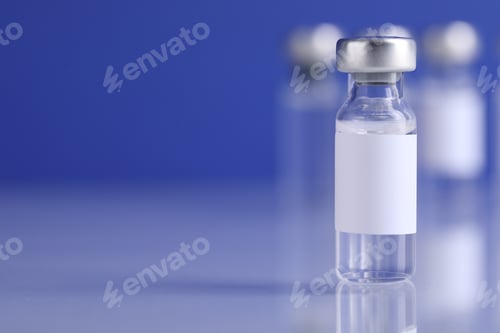 Preview: Vaccine in vial on light mirror surface against blurred blue background, closeup. Space for text