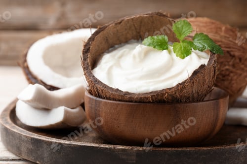 Preview: Tasty coconut yogurt with melissa leaves in shell and nuts on white table, closeup