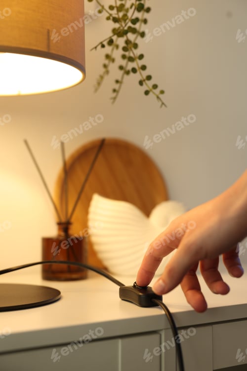 Preview: Woman turning off lamp with inline cord switch on shelving unit near white wall at home, closeup