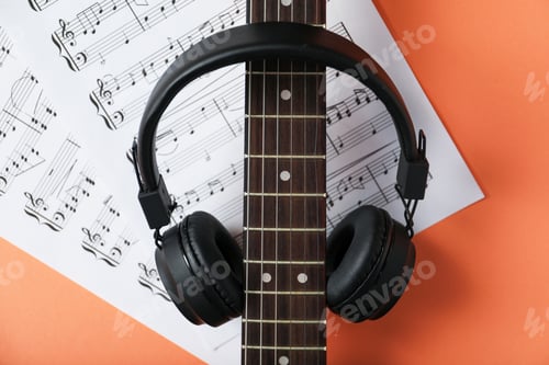 Preview: Headphones, music sheets and electric guitar on coral background, flat lay