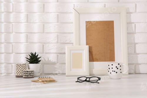 Preview: Stylish office workplace. Decor elements, glasses, cup and notebooks on white table near brick wall