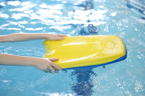 Preview: Little boy swimming with kickboard during lesson in pool, closeup