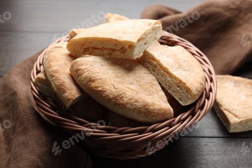 Preview: Pieces of tasty flatbread in basket and towel on wooden table, closeup