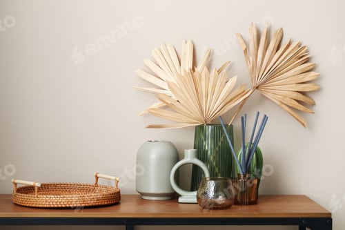 Preview: Beautiful vases and other decor on wooden table near beige wall indoors