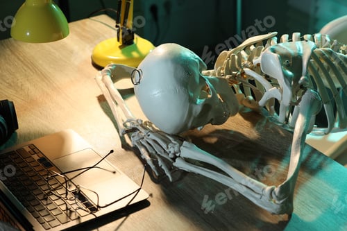 Preview: Waiting concept. Human skeleton sleeping at wooden table with laptop