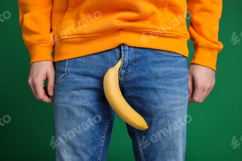 Preview: Urology. Man with banana in his pants on green background, closeup