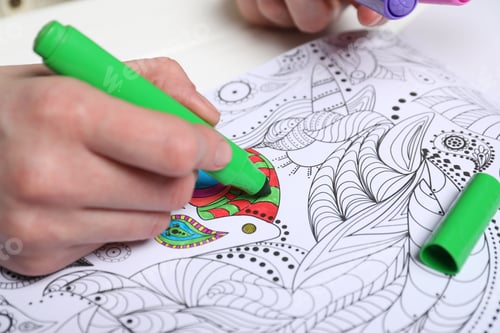Preview: Woman coloring antistress picture with felt tip pen at white table, closeup