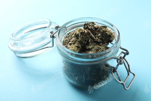 Preview: Dried medicinal herbs in jar on light blue background, closeup