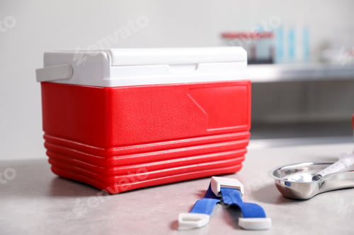 Preview: Cool box, medical tourniquet and syringe on grey table in clinic, closeup