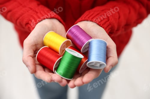 Preview: Woman holding spools of sewing threads indoors, closeup