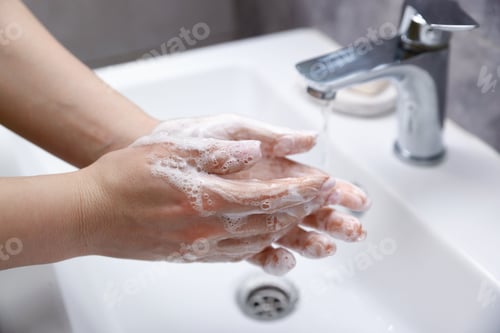 Preview: Woman washing hands with soap above white sink in bathroom, closeup