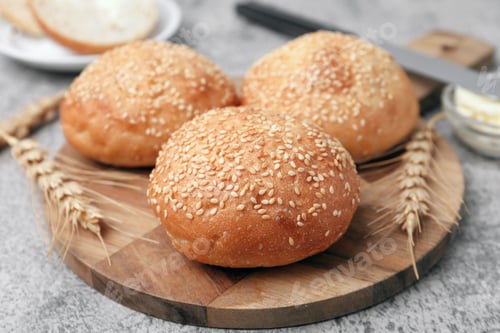 Preview: Yummy buns with sesame seeds and wheat ears on grey table, closeup