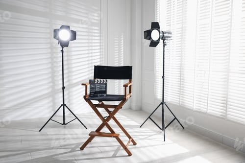 Preview: Film director's chair with clapperboard and lighting equipment in studio