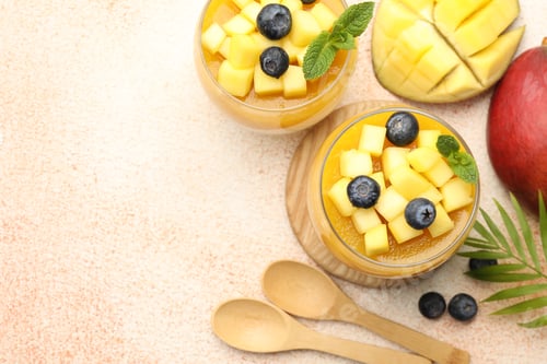 Preview: Delicious mango panna cotta with fruits and mint in glasses on beige textured table, flat lay. Space
