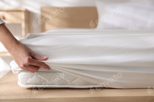 Preview: Woman putting bed sheet on mattress indoors, closeup