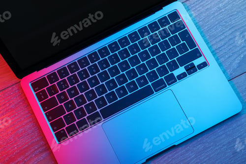Preview: Stylish modern laptop in neon lights on wooden table, top view