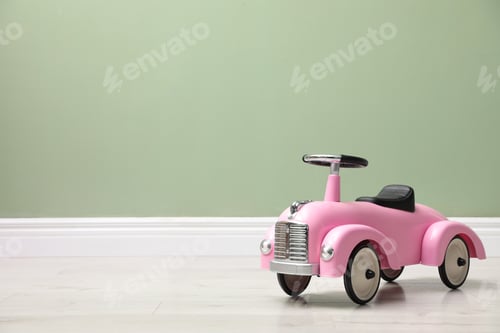 Preview: Pink toy car near light green wall indoors, space for text