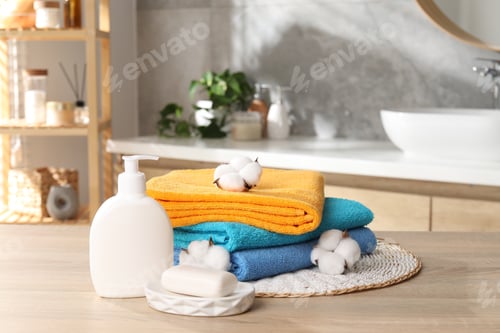 Preview: Stack of colorful towels, soap and cotton flowers on wooden table in bathroom