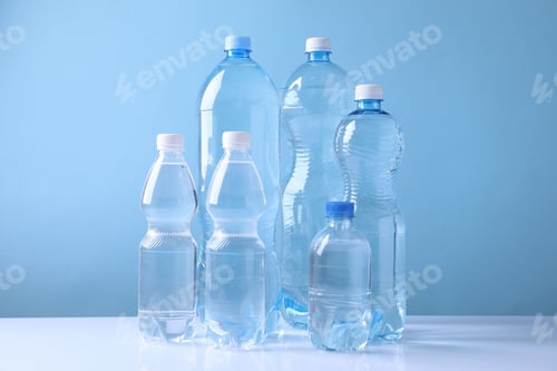 Preview: Water bottles of different sizes on white table against light blue background