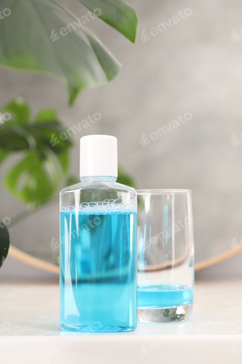 Preview: Bottle of mouthwash and glass on white table in bathroom